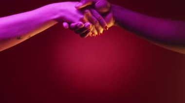 Çeşitli tokalaşmalar. Cinsiyet eşitliği. Uluslararası birlik. Pembe, neon ışıklı, çok kültürlü çift elleri kırmızı spot ışıklarının altında, karanlık arka planda..