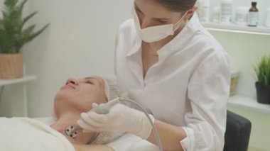 Kırışıklık yenileme prosedürü. Kadın güzelliği. Cilt bakımı. Boyun bölgesine profesyonel masajcı orta yaşlı kadın. İç mekânda donanım var..