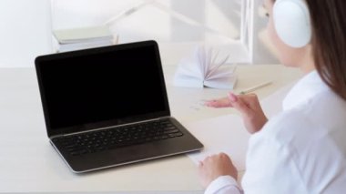 Çevrimiçi koçluk. Boş ekran. E-öğrenme dersi. Uzaktan eğitim. Kulaklıklı tanınmayan bir kadın laptop kullanarak siyah ekranı kopyalayarak öğretmenlik yapıyor. Uzun video çekimi.