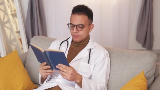 学习疲劳 职业失眠症卫生保健教育 厌倦了的男医生实习生在现代家居生活的沙发上看书 学习如何入睡 — 图库视频影像