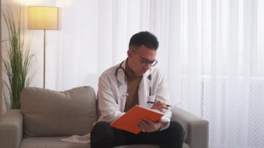 Tıbbi kayıtlar. Sağlık sigortası reçetesi. Hastane evrakları. Erkek doktor, modern iç mekândaki kanepenin panosuna doldurma belgesi yazıyor..