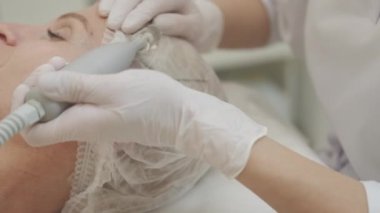 Güzellik bakımı. Rahat kadın. Drenaj prosedürü. Profesyonel kozmetoloji yüz gerdirme masajı, orta yaşlı bir bayanın aydınlık odada özel bir donanım cihazı kullanması..