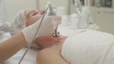 Kaldırma prosedürü. Kadın güzelliği. Cilt bakımı. İç mekanında donanım cihazı olan orta yaşlı bir kadın için profesyonel masaj boyun bölgesi..