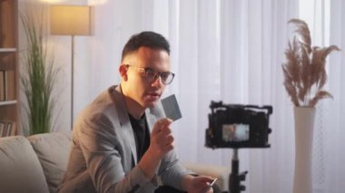 Dijital bankacılık. Video dersi için. Nakitsiz ödeme. Kendinden emin erkek vlogger modern iç mekanda kamerada kredi kartının sanal sunumunu kaydediyor..