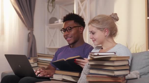 夫婦で勉強する オンライン研究 家庭教育 自由空間のリビングルームのインテリアでソファの上でノートパソコンの読書本を使用して熱狂的なスマート多様な学生 — ストック動画