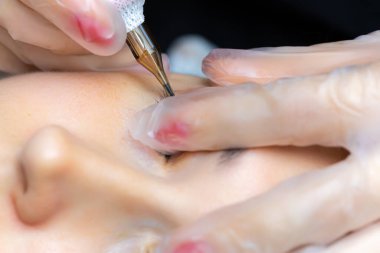 Dövmeci modelin göz kapaklarını esnetir ve kalıcı kirpik makyajı yapar.