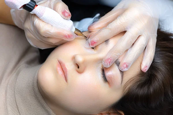 Dövmeci modelin göz kapaklarını esnetir ve kalıcı kirpik makyajı yapar.