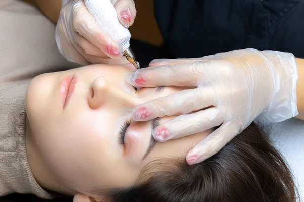 Dövmeci modelin göz kapaklarını esnetir ve kalıcı kirpik makyajı yapar.