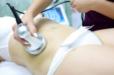 Kozmetik Ofisi 'nin uzmanı bir cihazın yardımıyla selülit ultrason tedavisi uyguluyor.