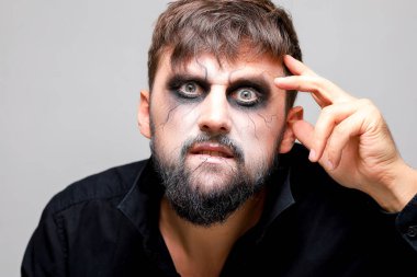 Ölümsüz makyajlı sakallı bir adamın portresi. Elini başının yanında tutuyor.