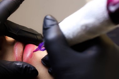 Dövmecinin yakın çekimi modelin dudaklarını iki parmağıyla gerdi ve alt dudağının dövmesini yaptı.