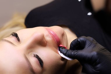 Modelin dudaklarındaki fazlalık pigmentleri pamuk süngerle silen usta bir dövme sanatçısının elleri.