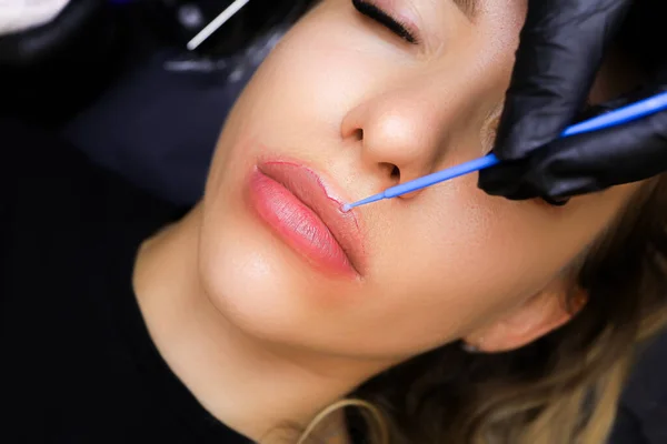the tattooist applies anesthesia to the contour of the model\'s lips with a small brush