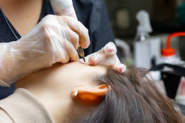 Kalıcı makyaj ustası yatağın başına oturur ve göz kapağı dövmesi prosedürünü uygular.