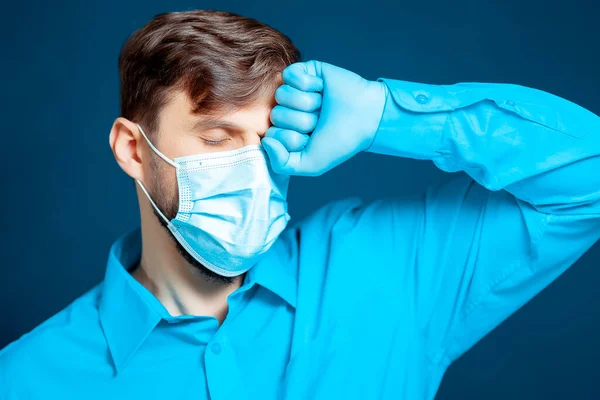 Tıbbi Maskeli Eldivenli Bir Doktor Mavi Üniformalı Yumruğunu Kafasına Dayadı — Stok fotoğraf