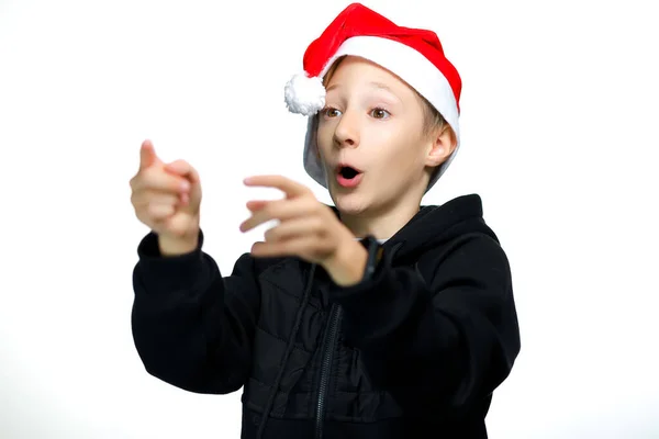那位戴圣诞老人红帽子的男孩用他的手展示了侧面 — 图库照片