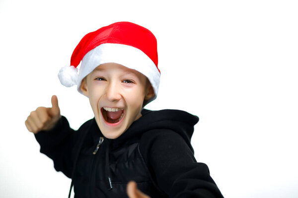 веселый мальчик в красной шляпе Санты стоит на белом фоне и весело смеется