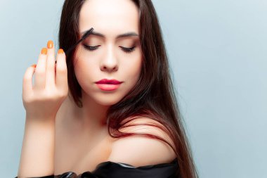 Genç ve güzel bir esmer model aşağıya bakar ve kaşlarını fırçayla tarar.