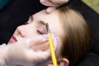 Usta, modelin kaşlarının üzerinde fırçayla kaplama kaşlar için ilk bileşimi dağıtır.