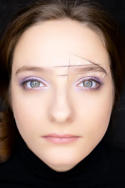 a model girl with open eyes lies on the eyebrow marking procedure