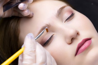 Usta, modelin kaşlarının üzerinde fırçayla kaplama kaşlar için ilk bileşimi dağıtır.