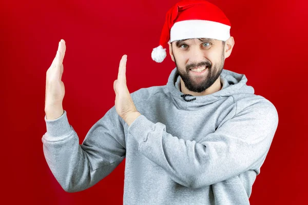 Человек Красной Шляпе Санта Клауса Красном Рождественском Фоне Показывает Своими — стоковое фото