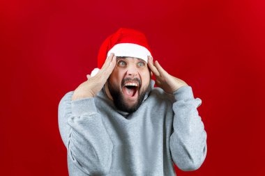 Kırmızı Noel Baba şapkalı bir adam kırmızı arka planda başını tutup bağırıyor.