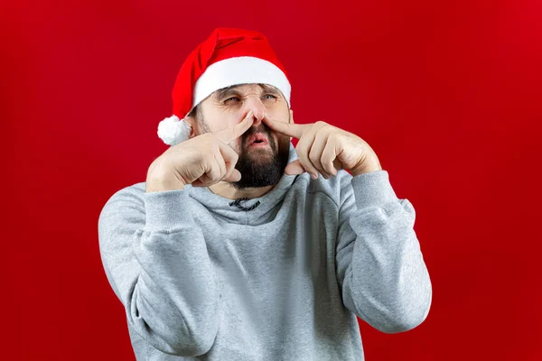 Kırmızı Bir Noel Arka Planında Sakallı Bir Adam Parmaklarıyla Burnunu — Stok fotoğraf