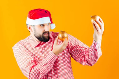 Noel Baba şapkalı ve kırmızı kareli gömlekli bir adam yeni yıl oyuncaklarını dikkatle inceliyor. Altın renkli bir top..