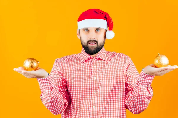 Ein Bärtiger Mann Mit Weihnachtsmütze Vom Weihnachtsmann Hält Goldene Spielzeugkugeln — Stockfoto
