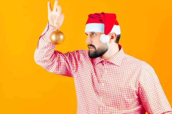 산타클로스의 모자를 남자와 셔츠를 남자가 새해의 장난감인 황금색 살펴보고 — 스톡 사진