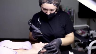 Usta modelin önünde oturur ve kaş dövmesi yaptırır..