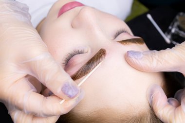 Modelin kaşlarının makro fotoğrafçılığı üstlerine kaş boyası sürmüş ve boyanmış. Üstat, pamuklu çubukla kaş çevresindeki fazla boyayı çıkarmaya çalışıyor.