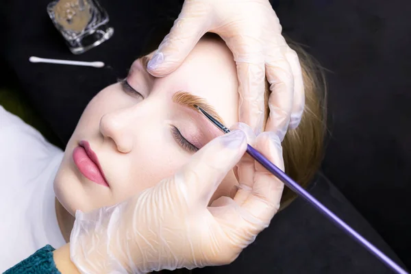 applying paint to the model\'s eyebrows with a brush after lamination