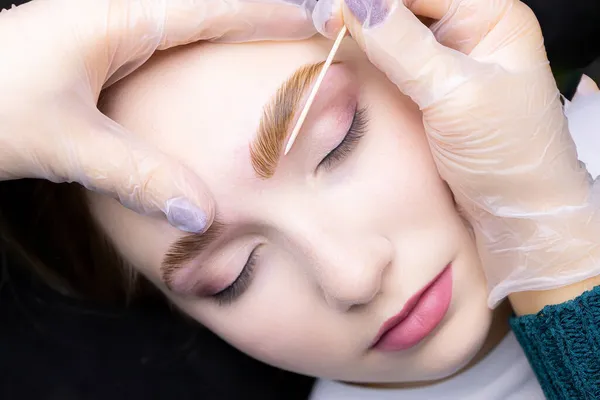 close-up alignment of the contour of the eyebrows with a cotton swab after the procedure lamination and coloring of the eyebrows