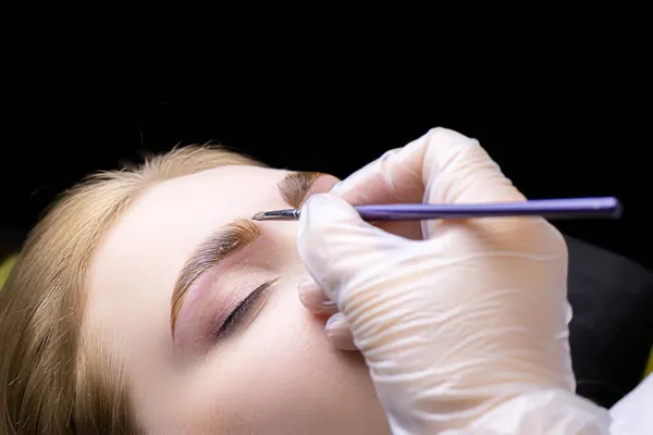 close-up of the eyebrows of the model on which the master applies a thick layer of paint for coloring the hairs of the eyebrows after lamination with compounds