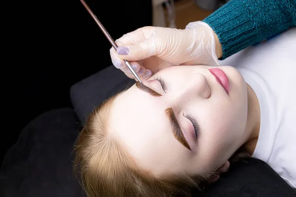 in the hands of the master, a thin brown brush with which he applies eyebrow paint to the hairs after the lamination procedure