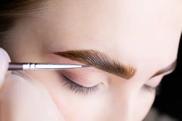 in the hands of the master, a thin brown brush with which he applies eyebrow paint to the hairs after the lamination procedure