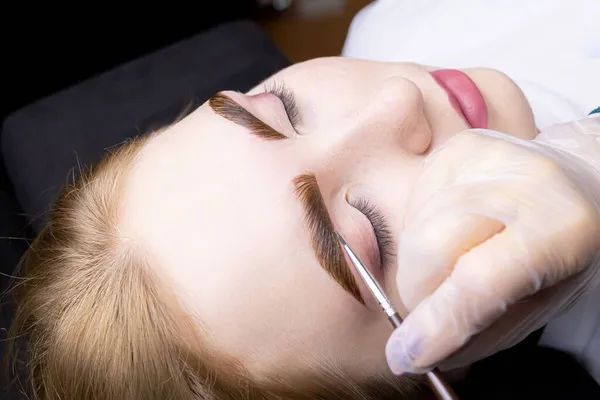 in the hands of the master, a thin brown brush with which he applies eyebrow paint to the hairs after the lamination procedure