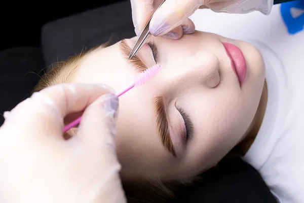 the master combs the eyebrows with a brush after the procedure of lamination and eyebrow coloring