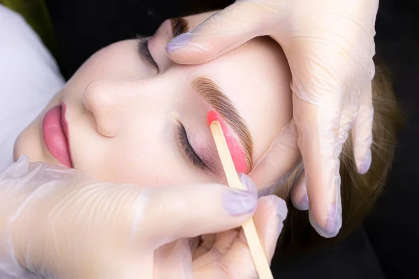 the hands of the master white gloves stretch the eyebrow of the model apply wax to remove unwanted hairs after the procedure of coloring and lamination