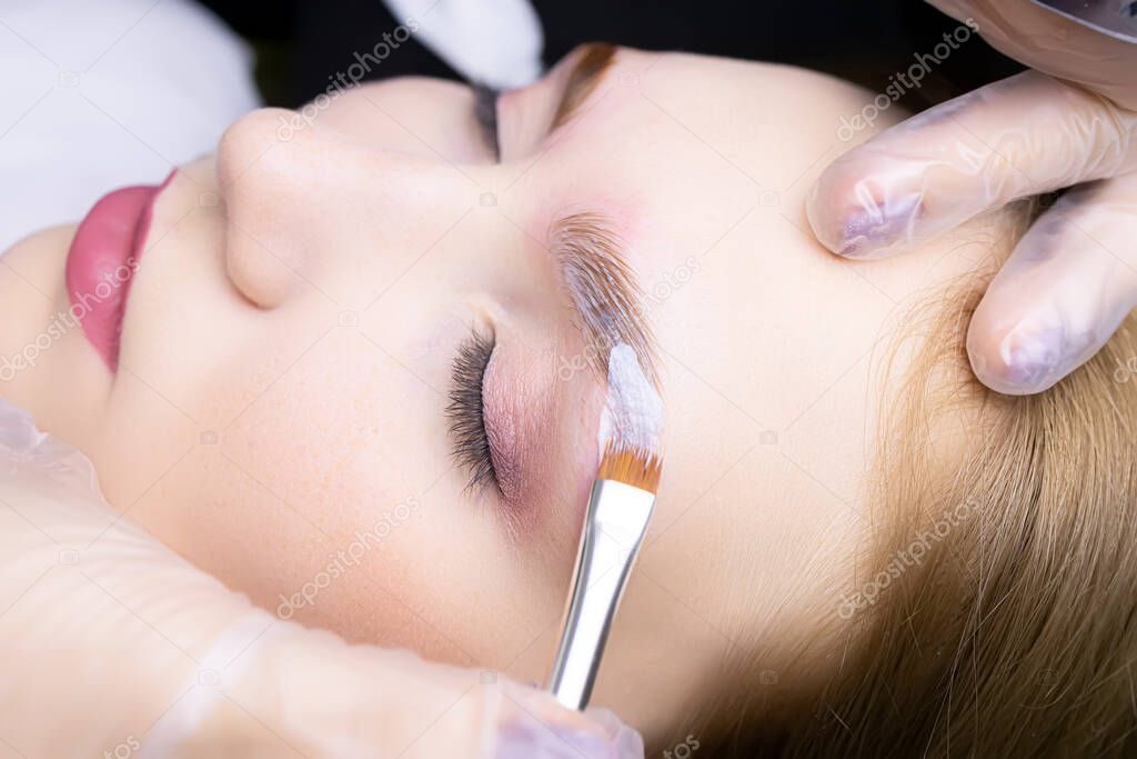 applying laminating compositions to the model's eyebrow in close-up using a brush