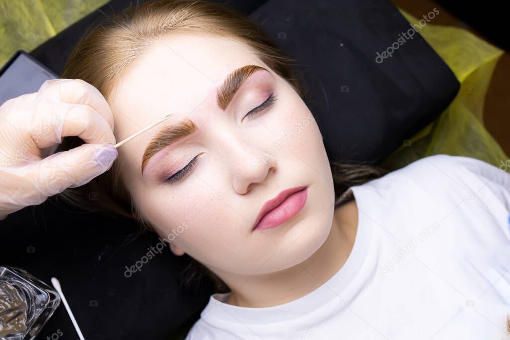 the face of a blonde model who is lying on the couch in a white T-shirt, with paint applied on her eyebrows