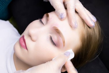 Kaş kaplama prosedüründeki kız model, üstat, pamuk süngerle kaplama bileşimlerinin kalıntılarını siler.