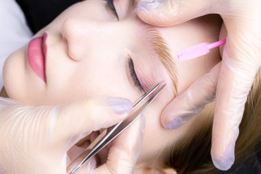 Kaş kaplama işlemi sırasında, usta kaş kıllarını cımbızla cımbızla alıyor.