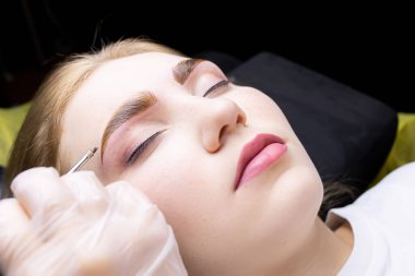 Modelin kaşlarına yakın çekim. Üstat, kaş kıllarını bileşiklerle renklendirmek için kalın bir boya tabakası uyguluyor.