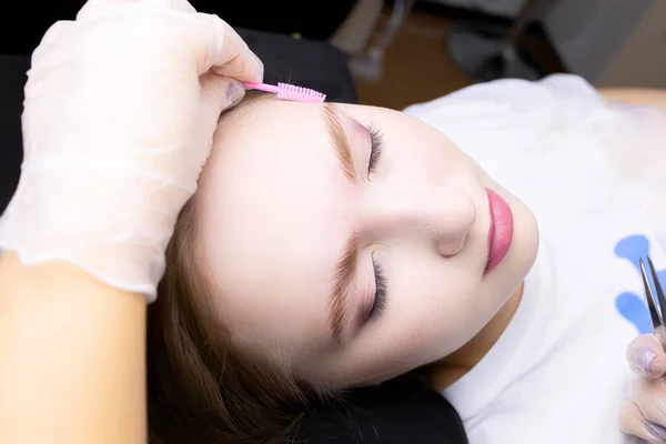 the model's face in close-up combs the model's eyebrows with a pink brush after lamination