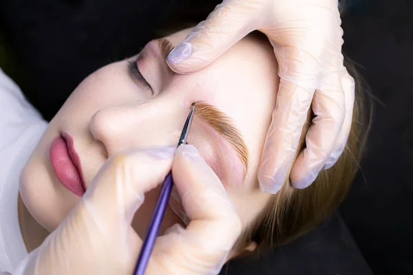 applying paint to the model\'s eyebrows with a brush after lamination