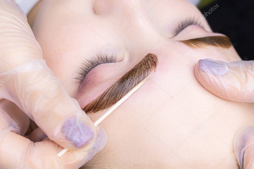 macro photography of the model's eyebrows painted and applied eyebrow paint on them, the master tries to remove excess paint from the contour of the eyebrows with a cotton swab
