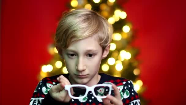 Een jongen zet op bril voor films op een Nieuwjaar Kerst achtergrond — Stockvideo